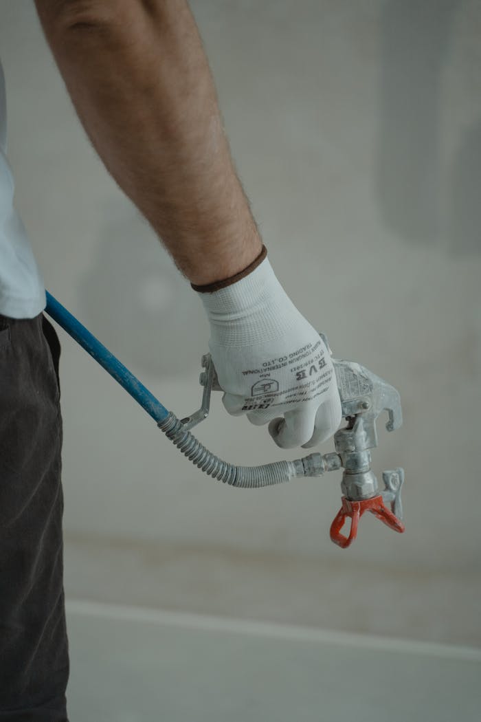 our-story-01 Arm of a worker holding a spray gun wearing gloves in an indoor setting, ready for painting.